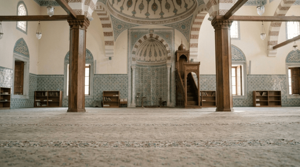 A man in a blue robe and white prayer cap prostrating on a prayer rug inside a mosque